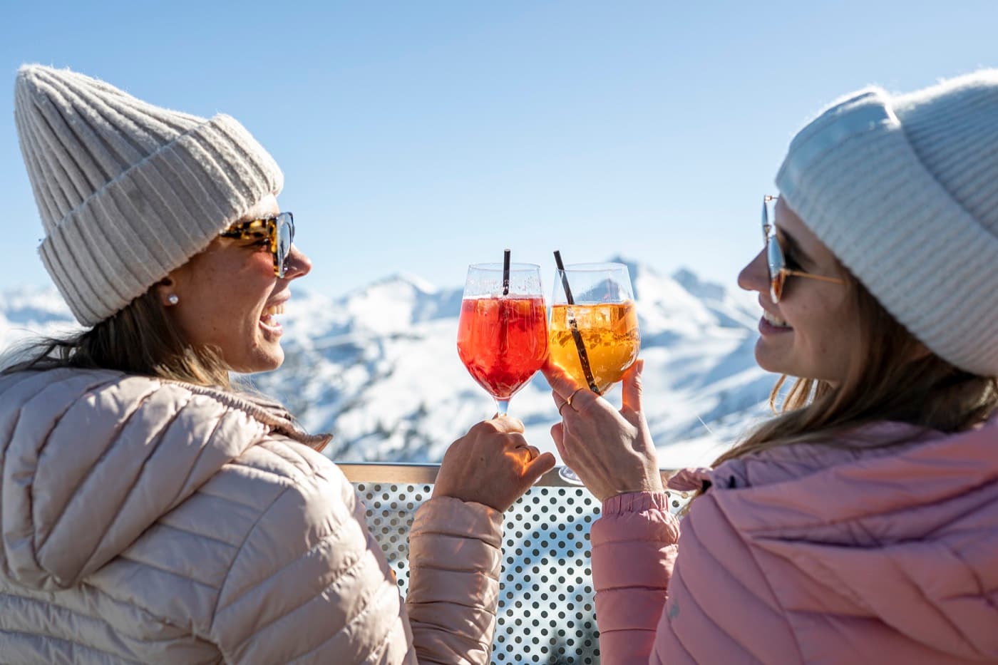 Zwei Gäste stoßen vor verschneiter Bergkulisse an