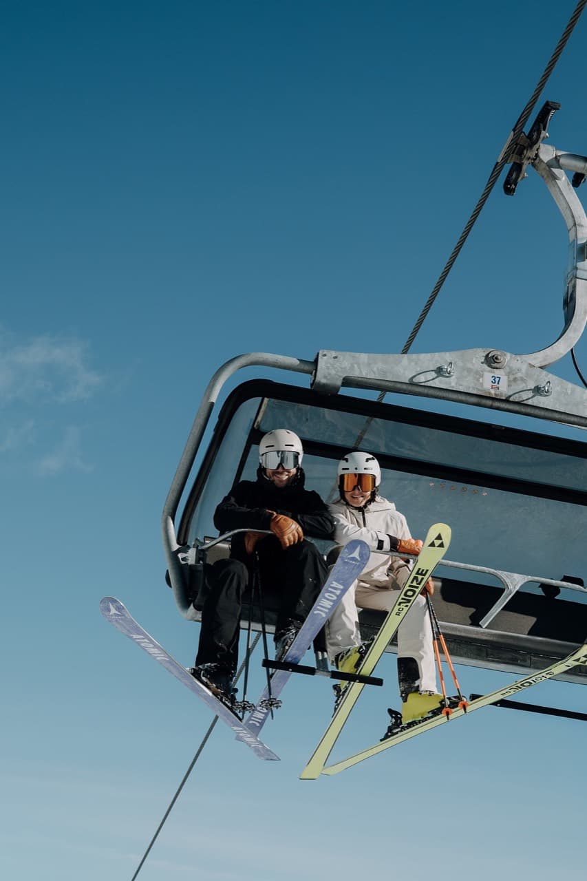 Zwei Skifahrer im Sessellift vor blauem Himmel